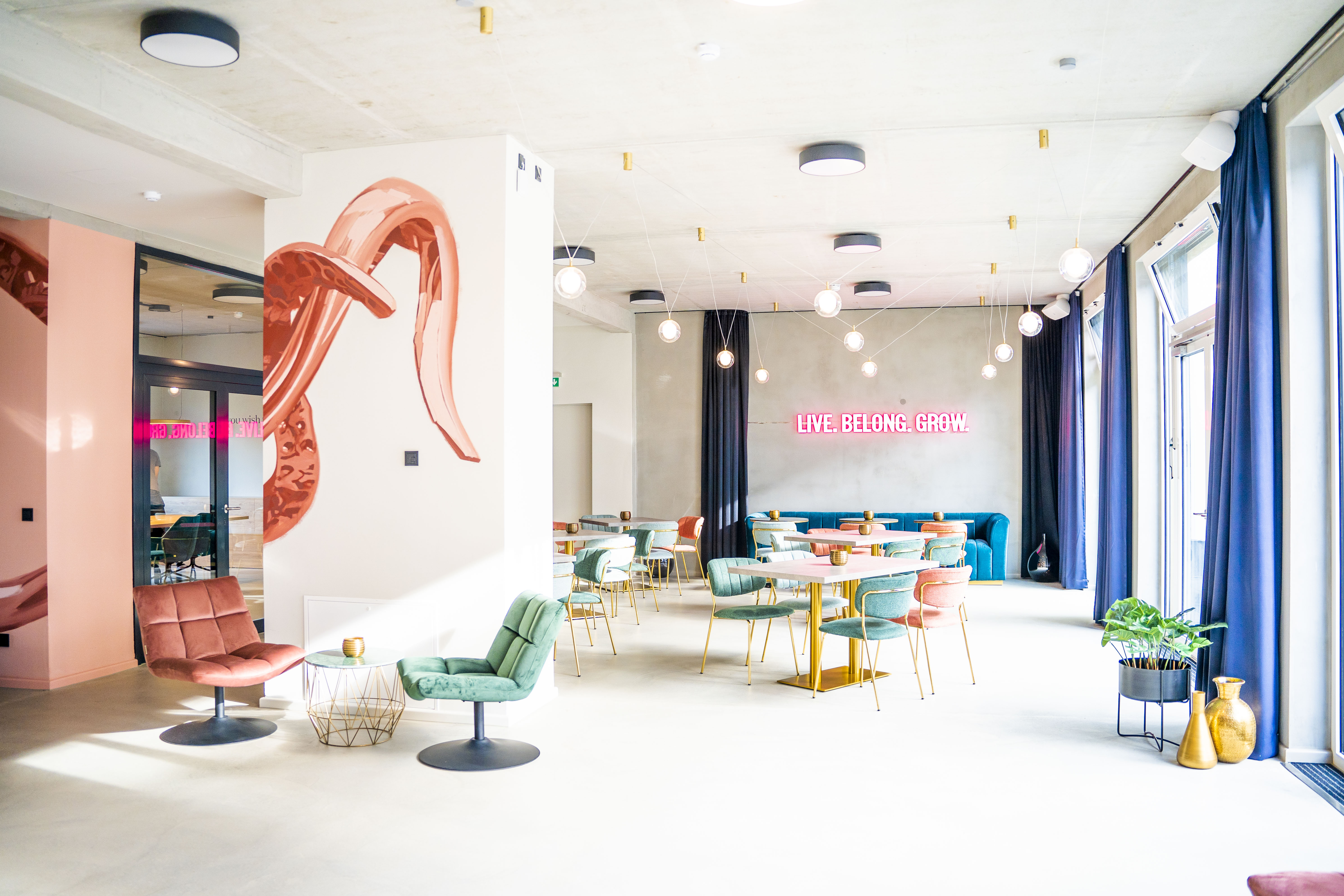 The Base Gemeinschaftsbereich mit bunten Sesseln aus Samt, einer Wandbemalung und Neonschild