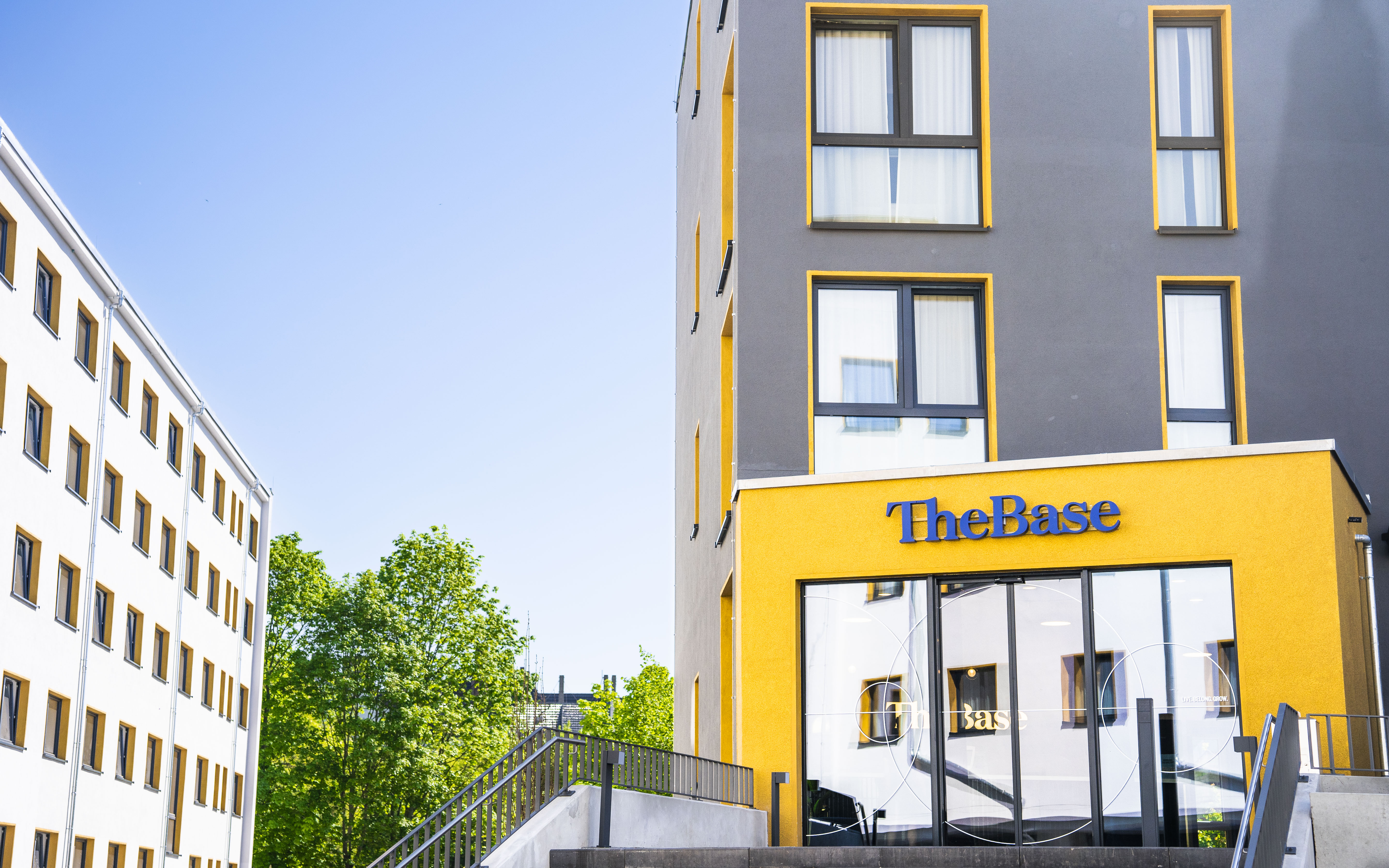 The Base Berlin Aussenansicht mit gelbem Eingang, Nebengebäude und Baum