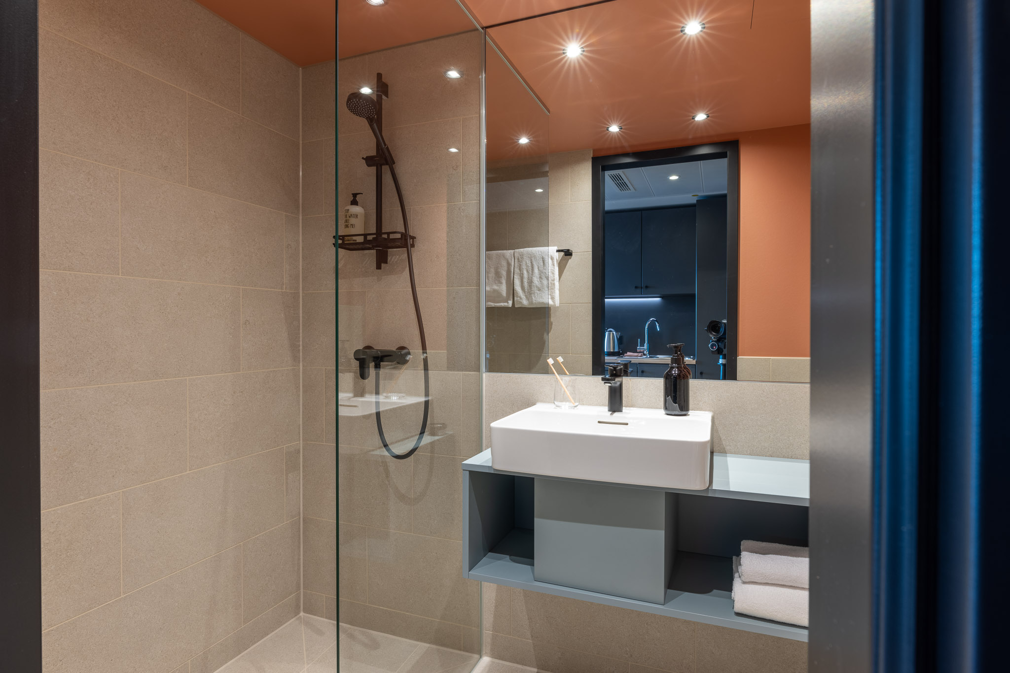 The Base Munich Badezimmer, Blick auf Dusche, Spiegel, Waschbecken und Waschtisch