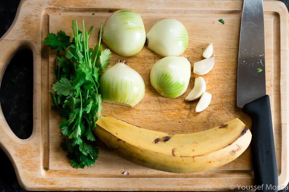 Plantain, onions, garlic and coriander ready to chop. Fry the plantains in the oil until golden and caramelised. Then remove and fry the onions and garlic afterwards.