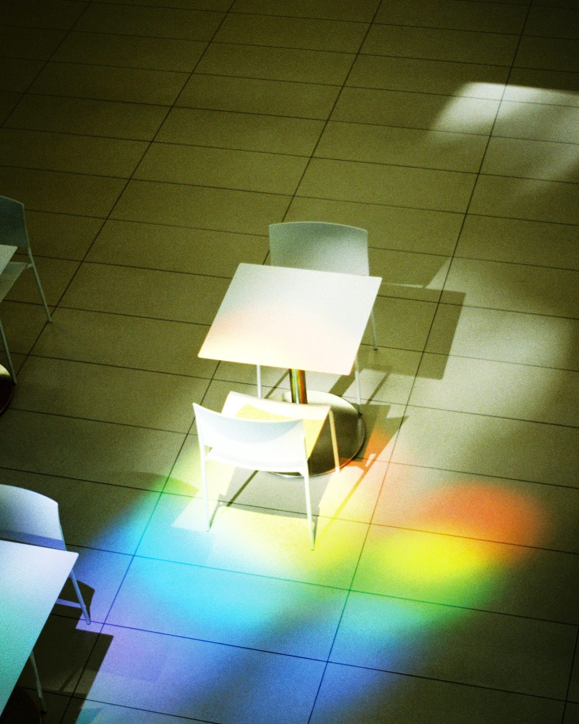 Overhead view of an empty modern cafe with white tables and chairs on tiled floor, illuminated by natural light and a rainbow reflection.