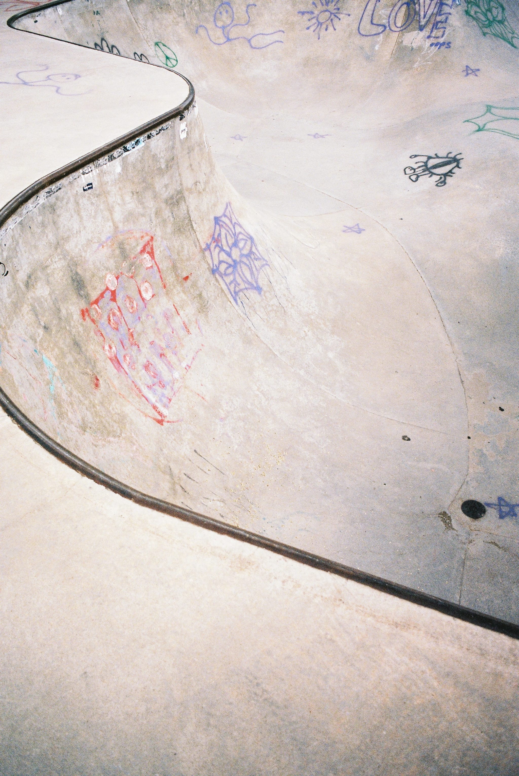 Aerial view of a concrete skatepark bowl with curved ramps, covered in colorful graffiti.