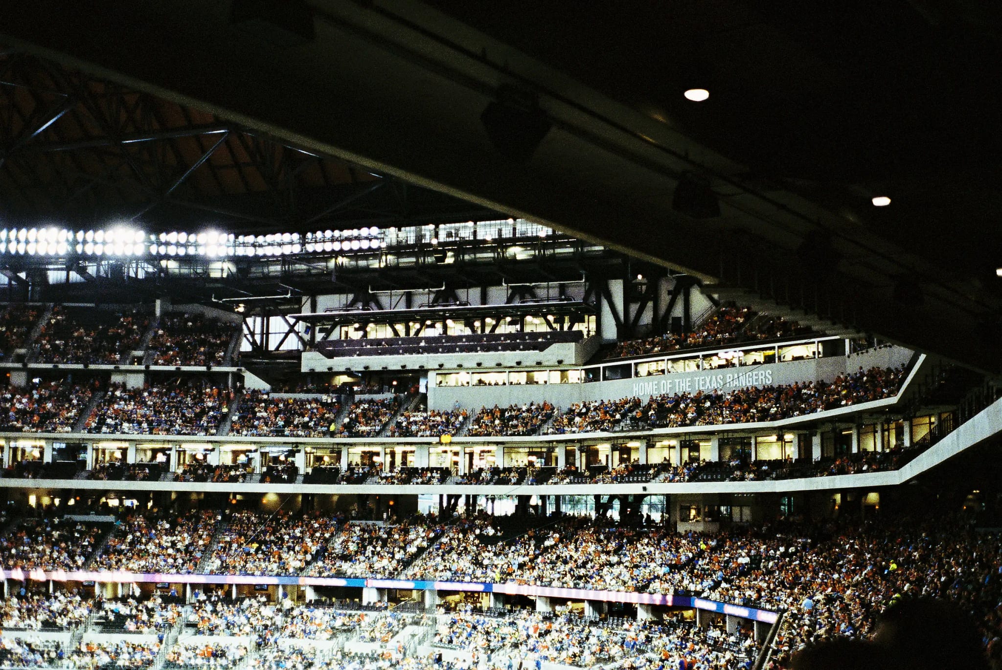 Globe Life Field interior during a game, crowd filling the tiers beneath the "Home of the Texas Rangers" sign.