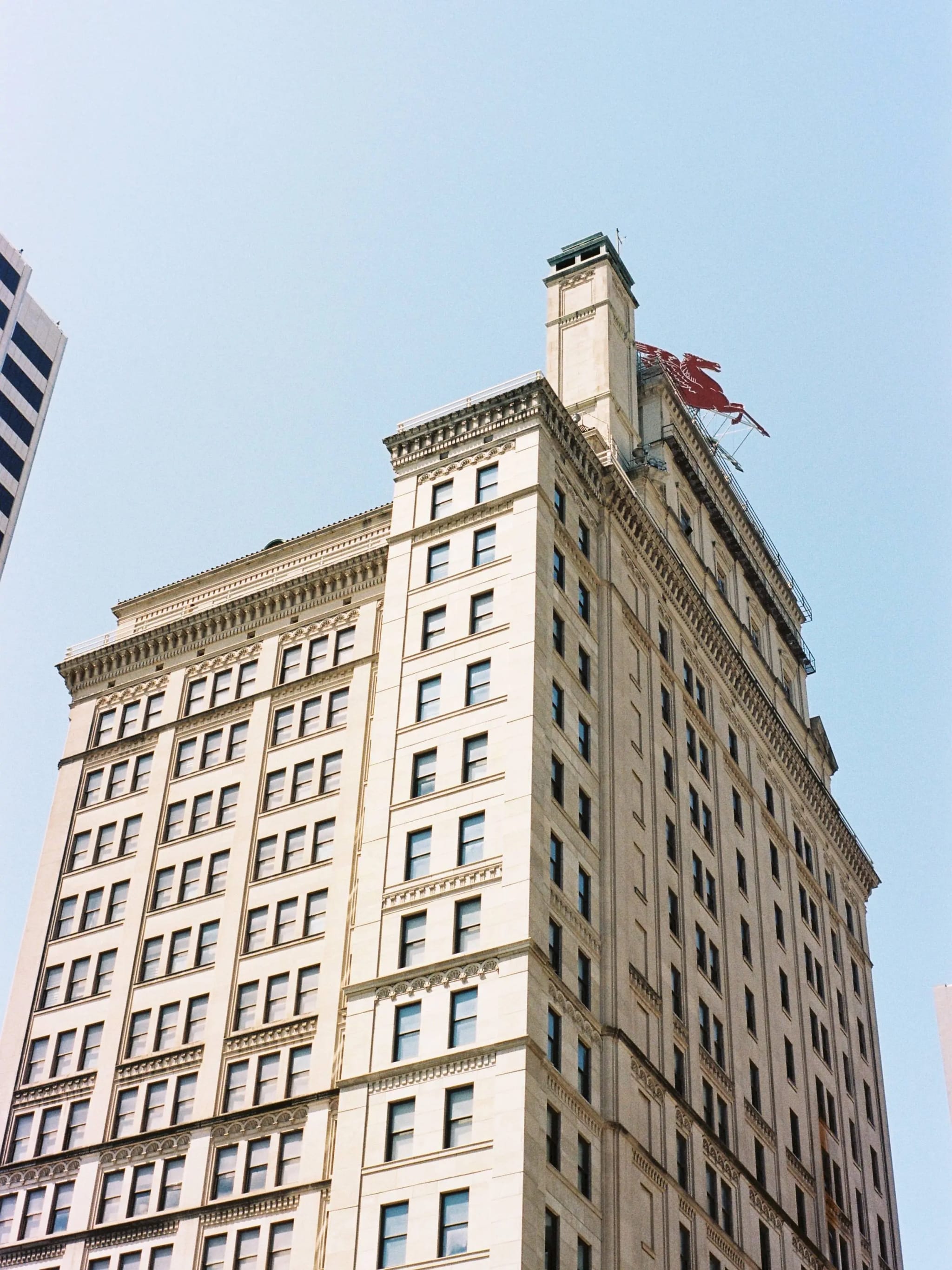 Historic Magnolia Building in Dallas photographed from below, featuring the red Pegasus rooftop sign against a clear blue sky.