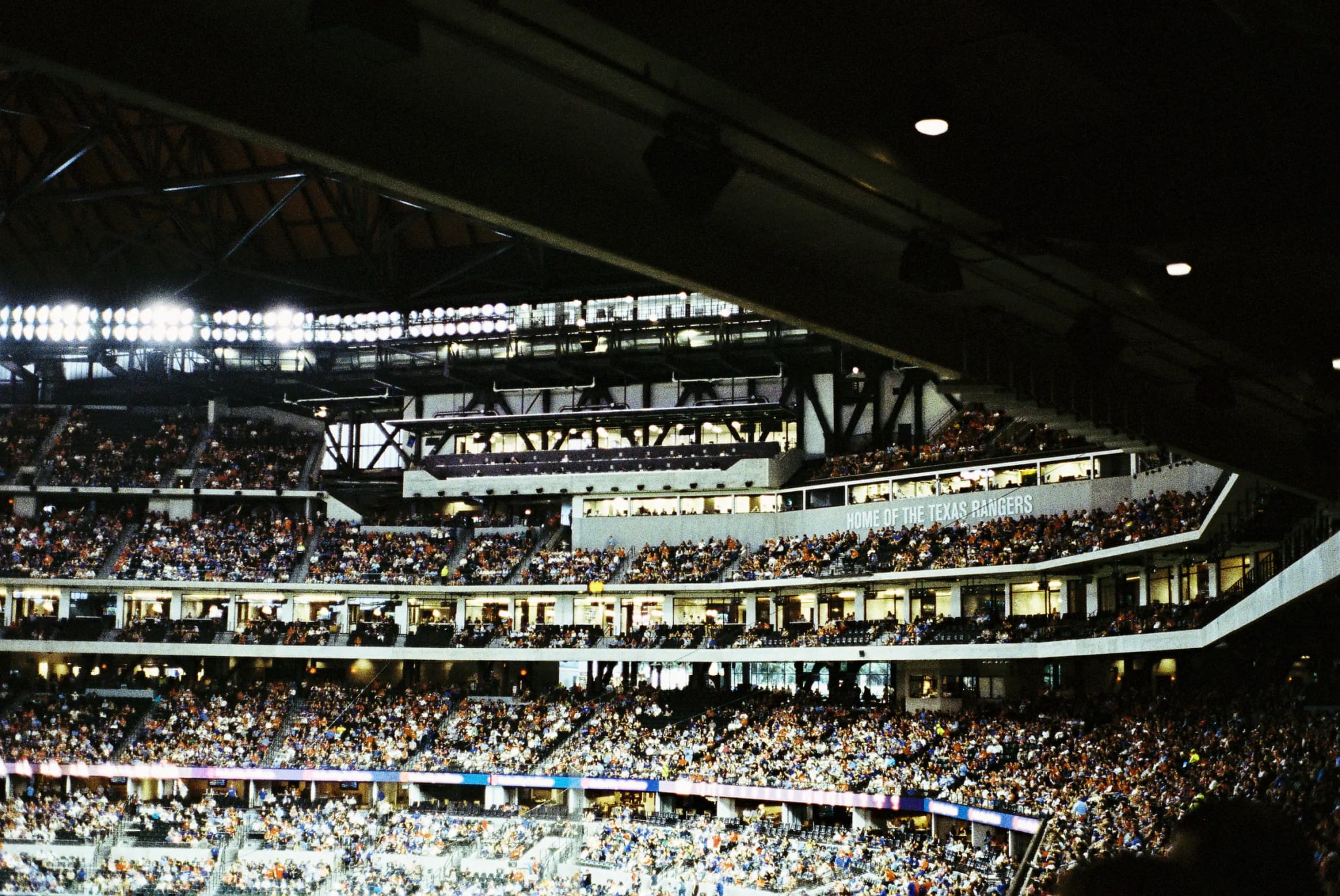 Globe Life Field interior during a game, crowd filling the tiers beneath the "Home of the Texas Rangers" sign.