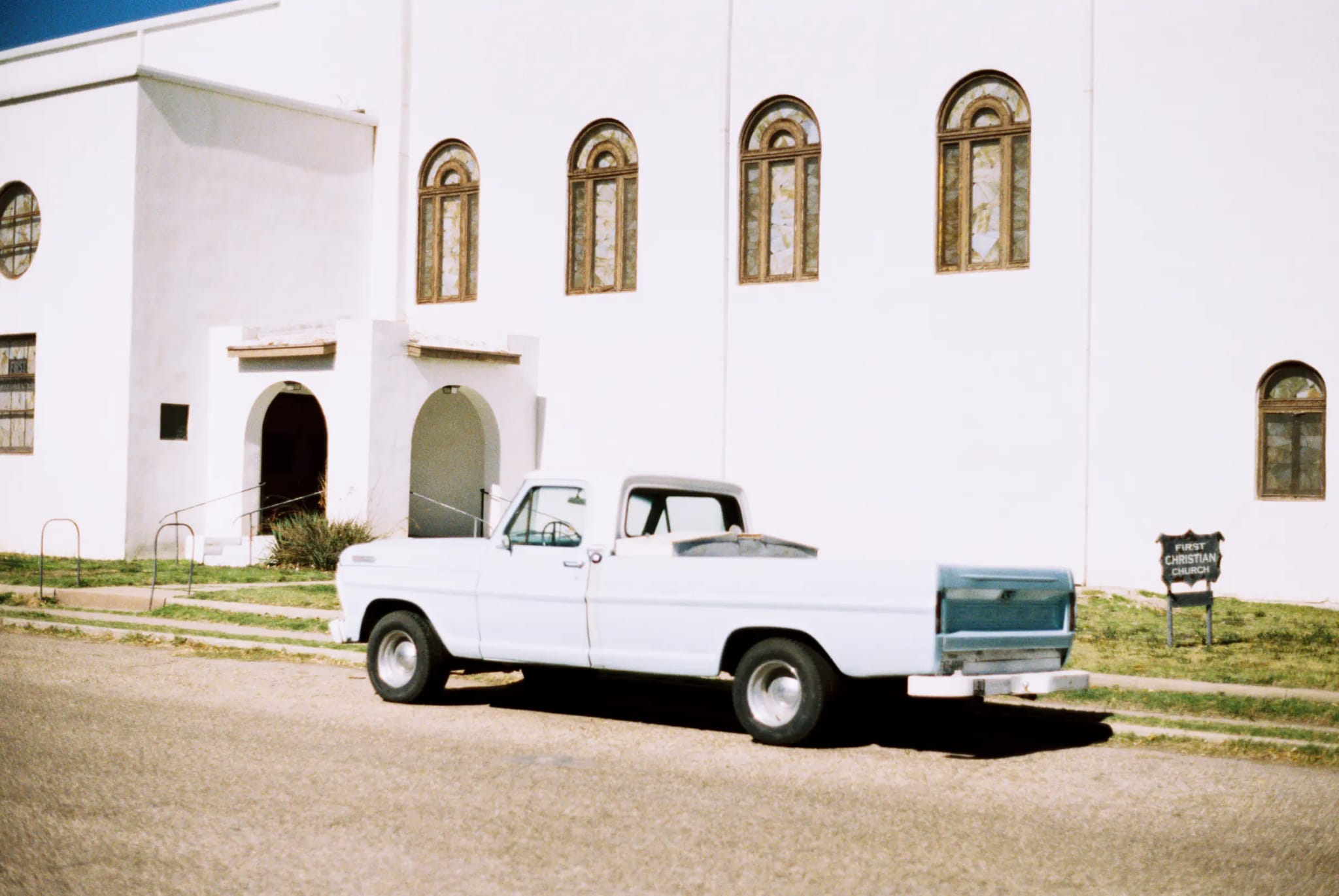 Vintage pickup truck parked beside a white church with arched windows.