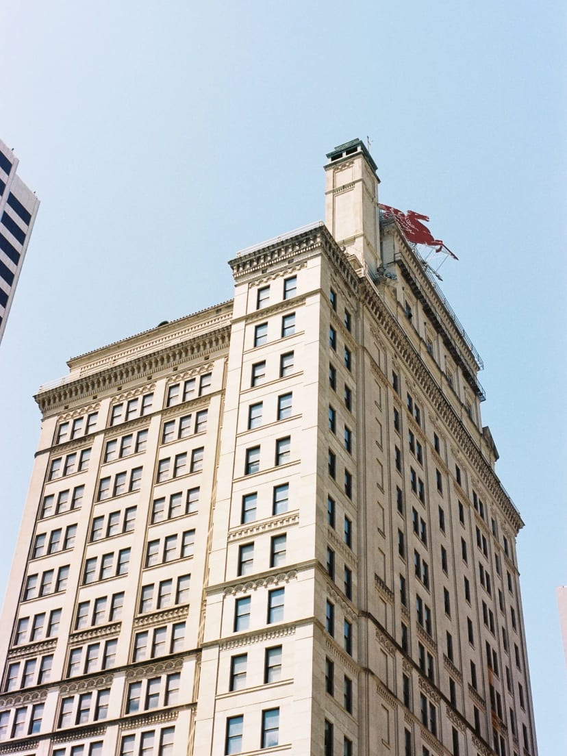 Historic Magnolia Building in Dallas photographed from below, featuring the red Pegasus rooftop sign against a clear blue sky.
