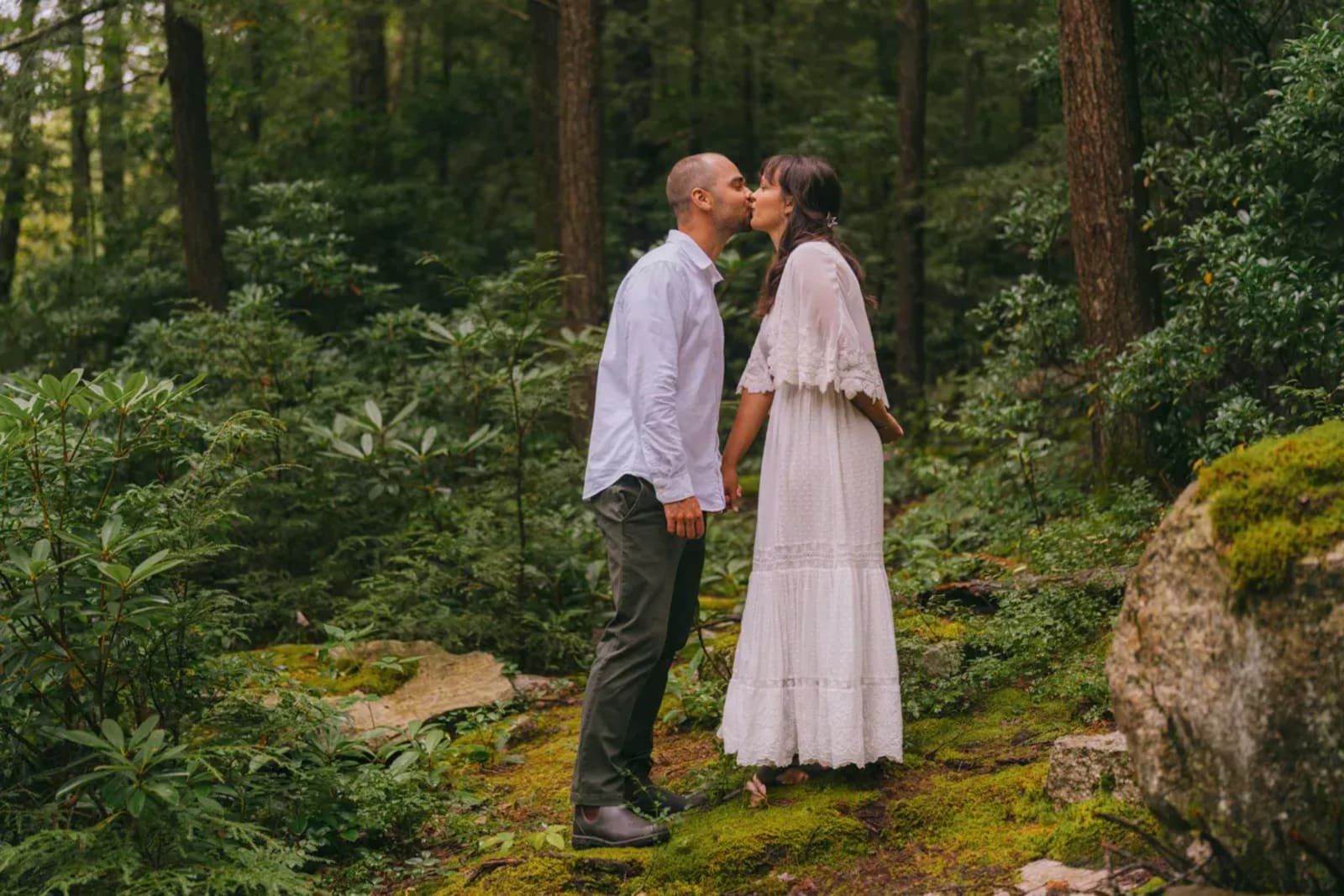Catskills elopement couple sharing a first kiss on moss-covered rocks in a lush green forest