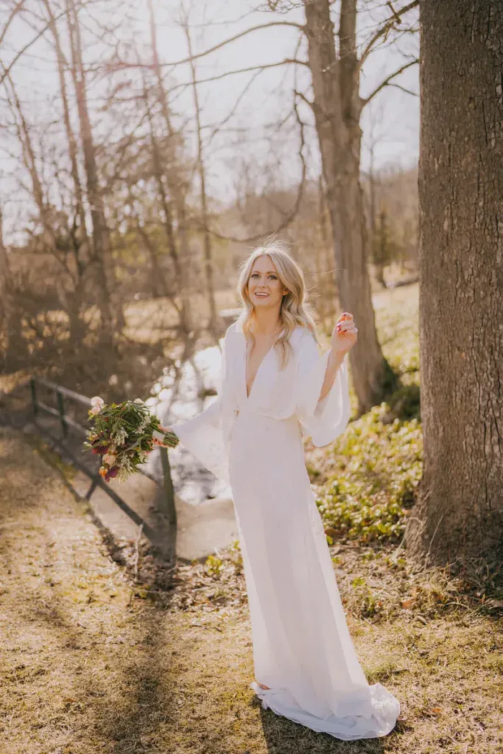 Hudson Valley elopement bride in a flowing white gown walking among spring trees with a wildflower bouquet