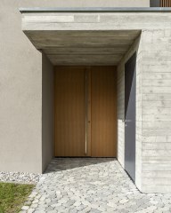 Eingangsbereich eines modernen Hauses mit Josko Haustür aus Holz, seitlicher grauer Nebentür und gepflastertem Weg.