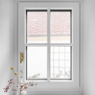 Weißes Sprossenfenster von Josko mit goldfarbenem Griff; auf der Fensterbank steht eine Glasvase mit getrockneten Zweigen und Beeren.