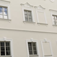 Ein frisch saniertes Stadthause mit heller Putzfassade, dekorativen Stuckrahmen und symmetrisch angeordneten, grau-weißen Fenstern von Josko im klassischen Stil.
