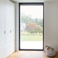 Helles Kinderzimmer mit großem Fixfenster von Josko mit Blick in den Garten, weißem Schrank und Korb mit Stofftieren auf hellem Fischgrät-Holzboden.