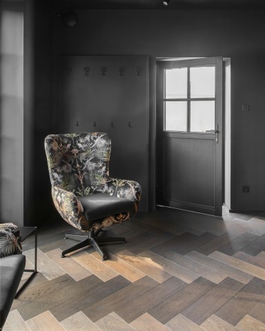Dunkle Nebeneingangstür von Josko mit Sprossenverglasung in einem modern gestalteten Wohnbereich mit dunklem Holzboden und gemustertem Sessel.