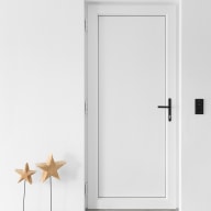 Schlichte weiße Nebeneingangstür von Josko, mit schwarzem Griff in heller Wand, daneben zwei dekorative Holzsterne.