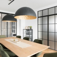 Moderner Essbereich mit großem Holztisch, gepolsterten Stühlen, zwei großen Hängeleuchten und raumhohen Schiebetüren mit schwarzem Metallrahmen und satiniertem Glas.