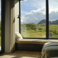 Schlafzimmer mit bodentiefen Holz/Alu-Fenstern von Josko und gemütlicher Sitzbank mit weitem Blick auf die grüne Berglandschaft.