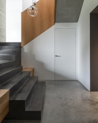 Innenansicht eines modernen Treppenhauses mit dunklen Steinstufen, Holzverkleidung am Geländer, weißer Josko MET Innentür und zwei runden Glaslampen.
