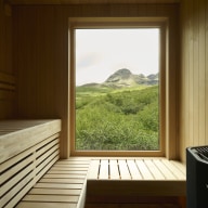 Holzverkleidete Sauna mit großem Holz/Alu-Fenster von Josko und freiem Blick auf die grüne Berglandschaft.