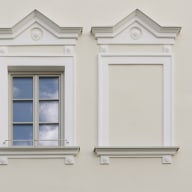 Detail einer hellen, historischen Fassade mit einem weißen Sprossenfenster von Josko und aufwendig gestalteten Stuckrahmen; rechts daneben ein geschlossenes, dekoratives Stuckfeld.
