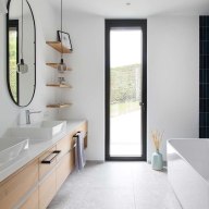Modernes Badezimmer mit Doppelwaschbecken, Holzunterschrank, bodentiefem Josko Fenster mit schwarzem Rahmen und heller Badewanne.