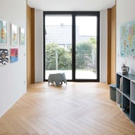 Helles Kinderzimmer mit großer schwarzer Josko Terrassentür Fischgrätparkett, bunten Bildern an der Wand, Spielzeugregal und kleinem blauen Elefant-Spielzeug.