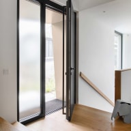 Moderne Eingangstür in schwarz von Josko mit schmalem Seitenteil aus Milchglas, geöffnet in einem hellen Vorraum mit Holztreppe und Parkettboden.