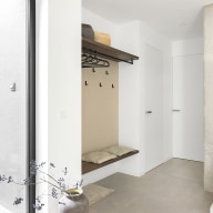 Minimalistischer Garderobenbereich mit weißer, mauerbündiger Innentür von Josko, links eine Holzbank mit darüberliegender beleuchteter Ablage, Haken mit Handtasche und Kleiderbügel, warmer Akzent durch eine dunkelrote Rückwand.