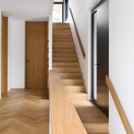 Innenansicht eines modernen Hauses mit Holztreppe und Türen in hellem Eichenholz, kombiniert mit weißen Wänden und einer schwarzen Josko Eingangstür.