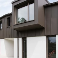 Moderne Hausfassade mit dunkelgrauer Metallverkleidung und markantem Erkerfenster von Josko über weißen Wänden, davor Garten mit Steinweg.
