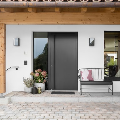 Einladender Eingangsbereich mit moderner Josko Haustür in elegantem Dunkelgrau und seitlichem Glaselement – stilvoll kombiniert mit natürlichen Materialien und liebevollen Details.