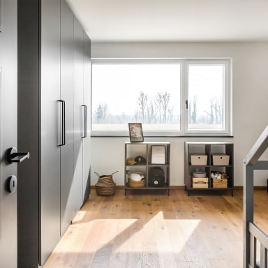 Helles Kinderzimmer mit großem, weißem Kunststoff/Alu-Fenster von Josko, Einbauschrank in Grau, Holzfußboden und Spielbereich mit Regalen und Kommode.