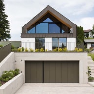Modernes Haus mit Satteldach, großer Glasfront von Josko und Balkon im Obergeschoss, darunter Garage mit breiter Einfahrt und seitlicher Treppe.