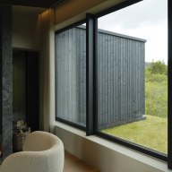 Wohnbereich mit großflächigen, dunklen Holz/Alu-Fenstern von Josko, die den Blick auf die Holzfassade und grüne Landschaft öffnen.