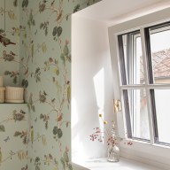 Helles Sprossenfenster von Josko in einem Raum mit mintgrüner Tapete mit Vogelmotiven; auf der Fensterbank steht eine Glasvase mit getrockneten Zweigen.