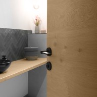 Geöffnete Innentür von Josko, aus Holz mit schwarzem Griff, Blick in ein modernes Badezimmer mit Waschtisch, dunklen Fliesen und dekorativer Beleuchtung.