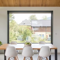 Moderner Essbereich mit Holztisch, weißen Stühlen und großer, schwarzer Fensterfront von Josko mit Blick ins Grüne.