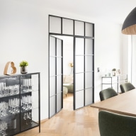 Moderner Essbereich mit Holzboden, Vitrine und großem Tisch, verbunden durch eine zweiflügelige Lofttür mit schwarzem Metallrahmen.
