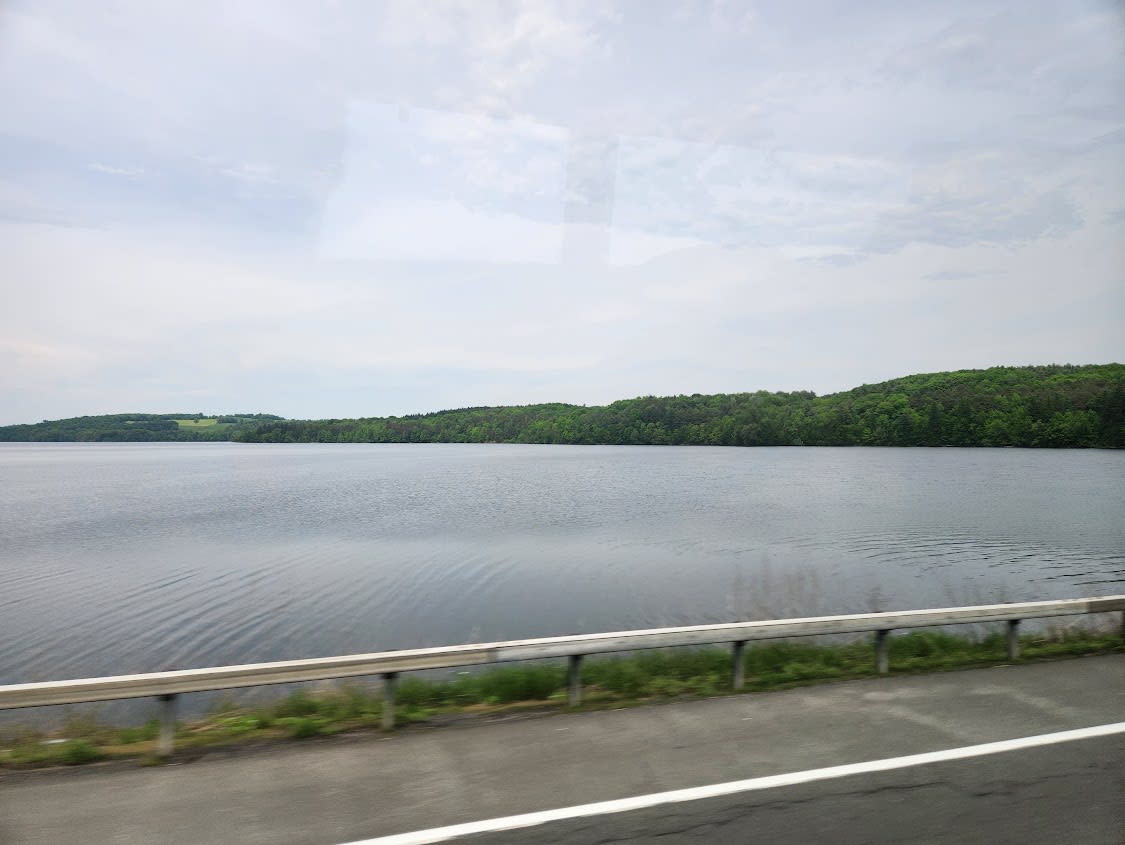 Driving alongside a calm lake on a cloudy day
