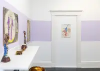 gallery installation of three drawings on a purple wall with sculptures on a mantle in the foreground