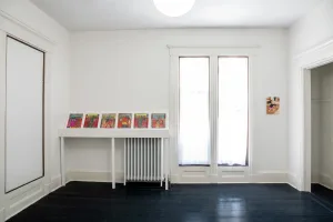 gallery installation of six drawings above a radiator and a small oil painting on the wall divided by a large bay window