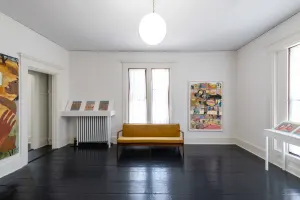long shot of a gallery installation featuring 6 artworks with a large bay window in between and a couch