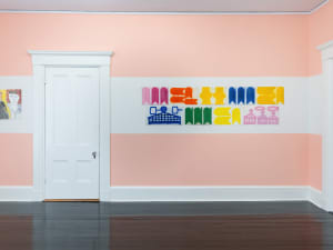 gallery installation of drawings and paintings on a wall with a door