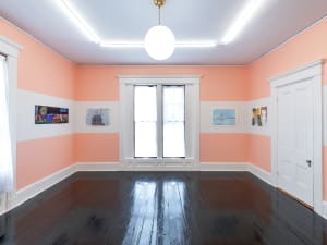long shot of four artworks with a window on a gallery wall