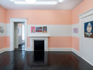 long shot of a gallery installation featuring six artworks and a fireplace