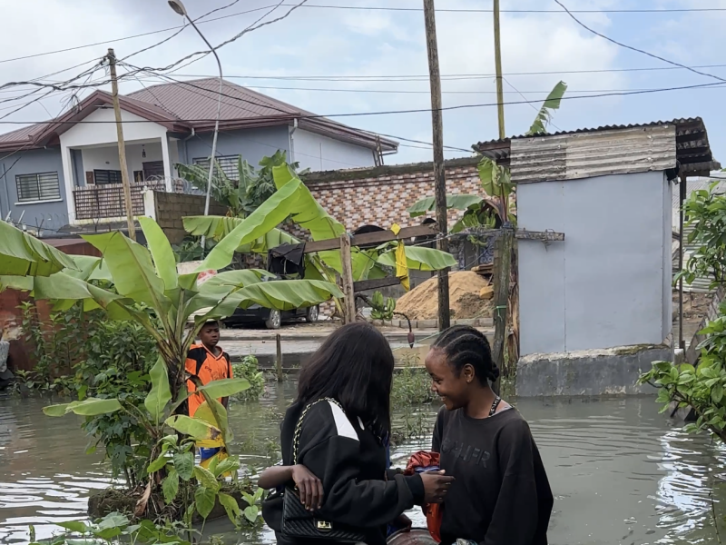 Two young women talk in a flooded street beside banana plants