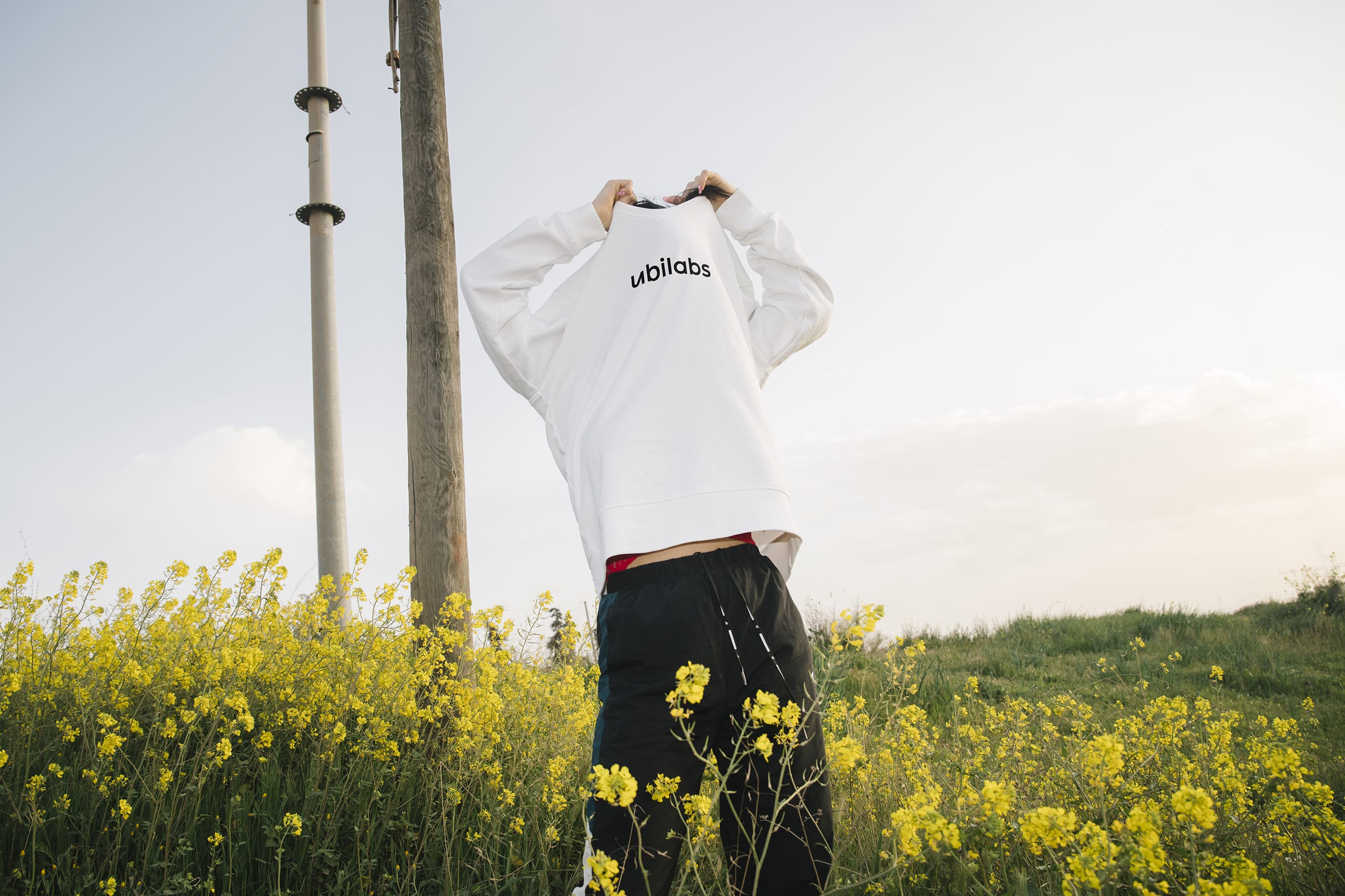 Logo platziert auf einem angezogenen Pullover. Person steht in einem Rapsfeld und im Hintergrund stehen zwei Masten.