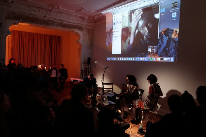 Lecture with wall projection of works from the exhibition. Several people are sitting in the audience.