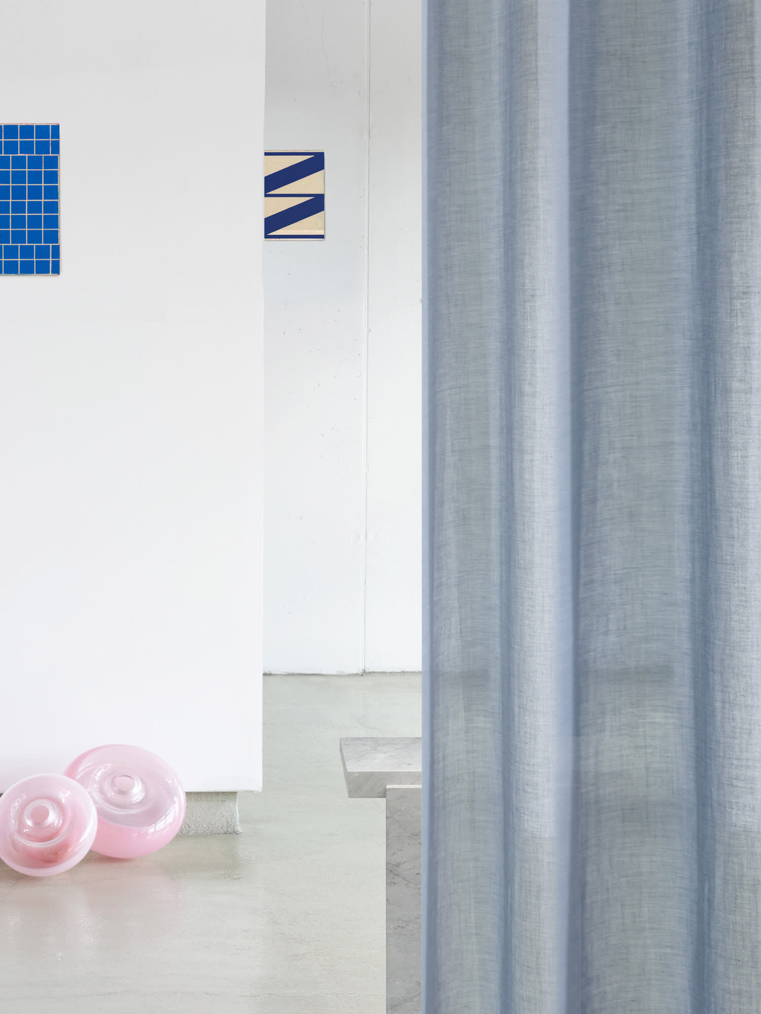 Kampagnenfotografie eines hellen Raumes mit einem blauen Vorhang im Vordergrund. Im Hintergrund sind weitere Stoffsamples zu sehen und auf dem Boden liegen rosane Lampenschirme.