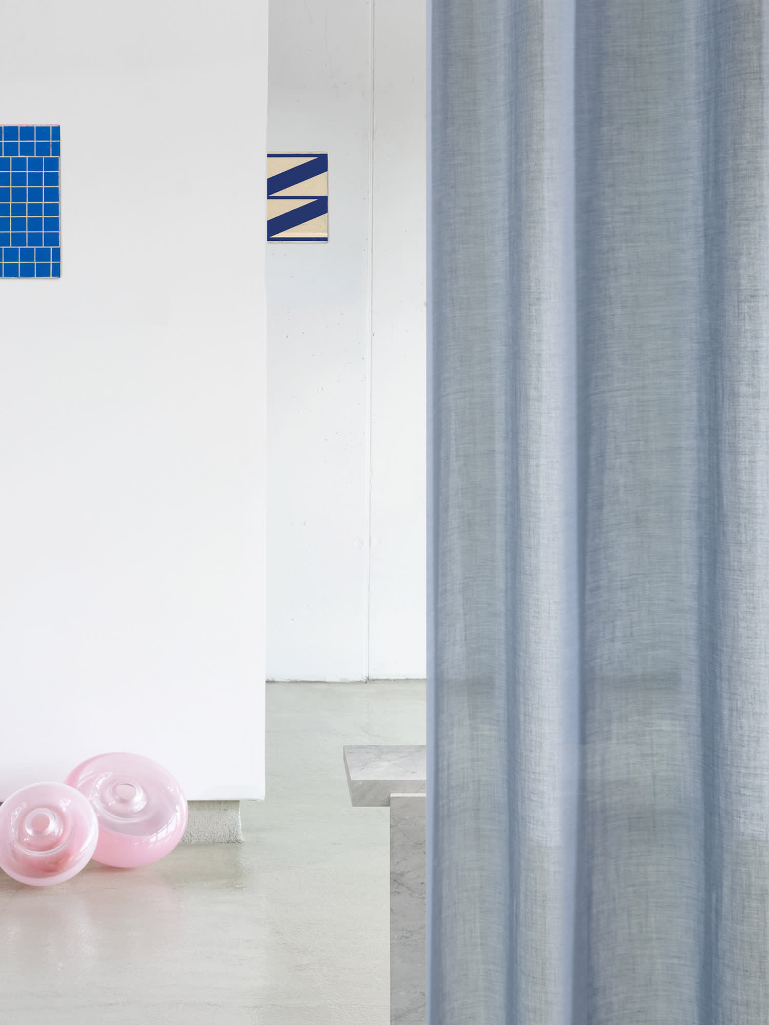 Campaign photography of a bright room with a blue curtain in the foreground. In the background are more fabric samples and on the floor are pink lampshades.